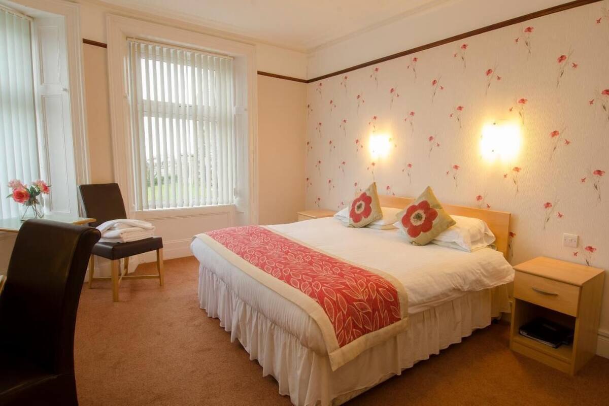 A neatly arranged bedroom with a large bed, two bedside tables, a chair, and a desk.