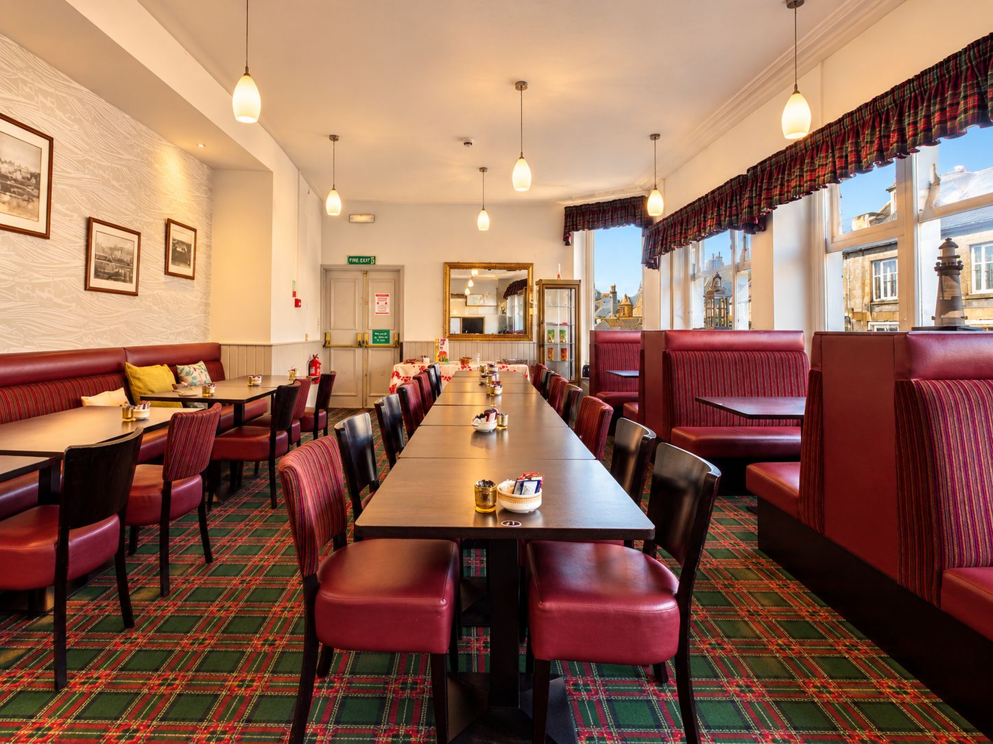 A hotel dining area with a long table, red upholstered booths, and patterned carpet.