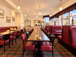 A hotel dining area with a long table, red upholstered booths, and patterned carpet.