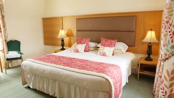 A hotel room with a large bed, two bedside tables with lamps, a chair with a green cushion, and a wooden headboard.
