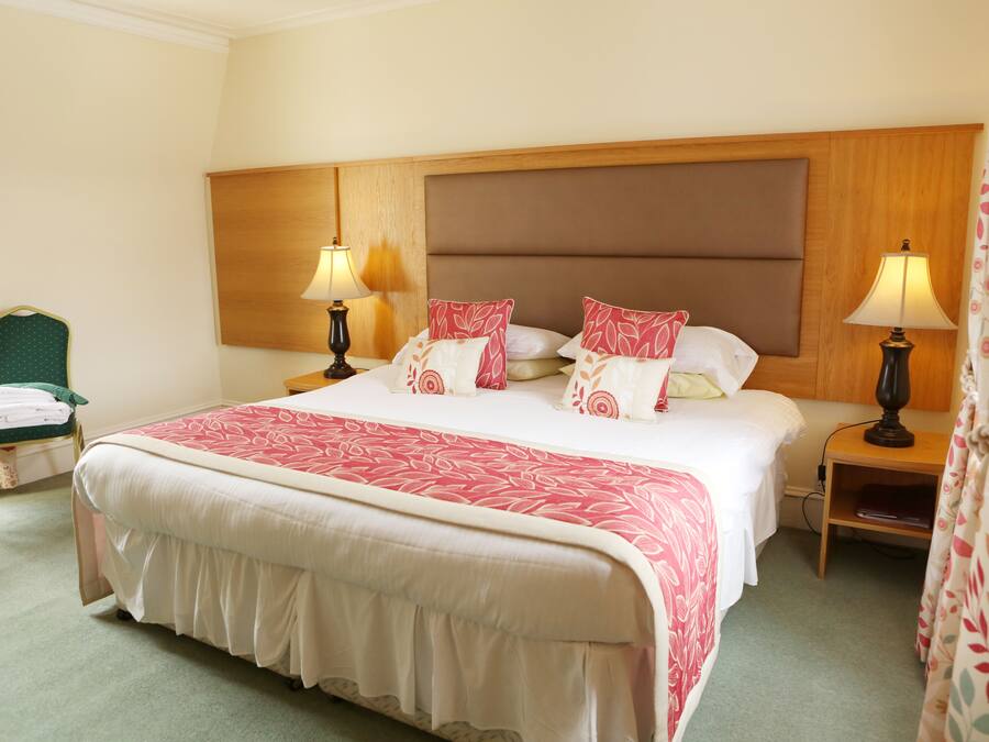 A hotel room with a large bed, two bedside tables with lamps, a chair with a green cushion, and a wooden headboard.
