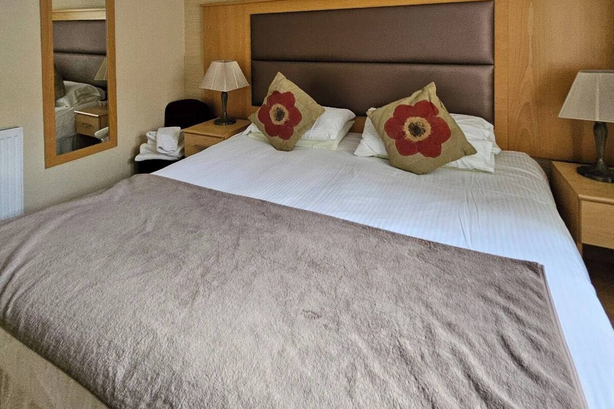 A hotel room with a large bed, two bedside lamps, a nightstand, a mirror, and a ceiling light fixture.