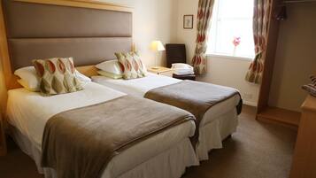 A hotel room with two beds, a desk, a chair, a lamp, and a window with curtains.