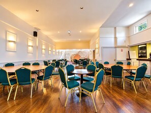 A hotel conference room with multiple tables and chairs, a kitchen area, and a view of the outdoors. - Homesly The Station Hotel (Banff)