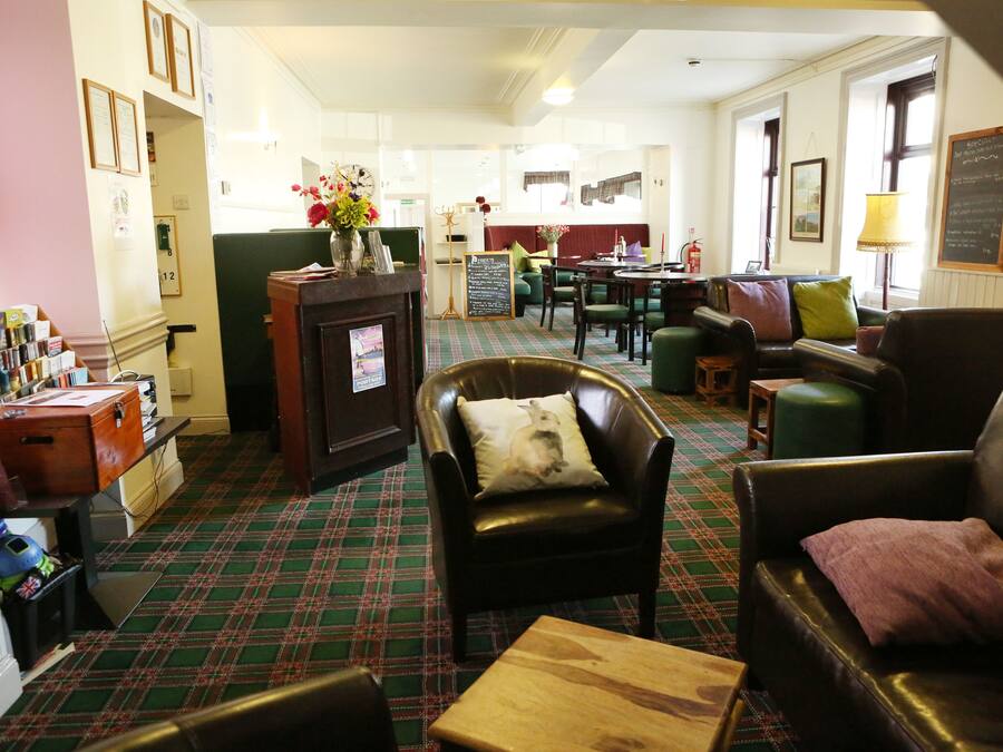A cozy hotel lobby with a plaid carpet, leather armchairs, a wooden coffee table, and a fireplace.