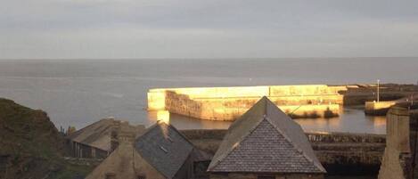 Una fortificación costera con edificios de piedra en primer plano y vista al mar.