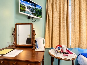 A hotel room with a wooden desk, a television mounted on the wall, a bed with a blue blanket, and a window with curtains. - Homesly The Station Hotel (Banff)