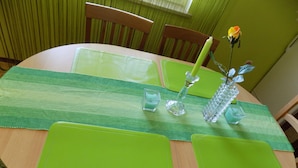 Una mesa de comedor con manteles individuales verdes, candelabros de cristal transparente y una rosa amarilla.