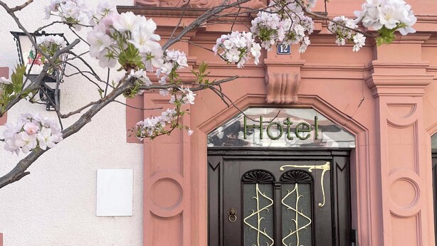 A hotel entrance with a black door, a sign above it, and pink architectural details. - Hotel Krokodil (Heidelberg)