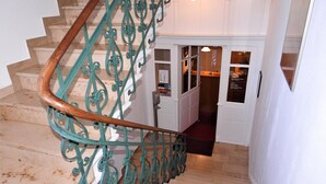 A staircase with a wooden handrail and green wrought iron balusters leading to a room with a door and a window. - Hotel Krokodil (Heidelberg)