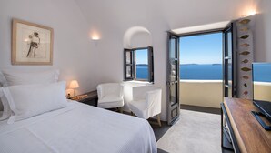 Habitación de hotel con cama, dos sillas, un escritorio y un ventanal con vista al mar.