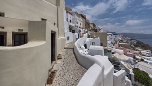 Una estrecha calle con paredes blancas y una pronunciada pendiente, que conduce a la costa con edificios y vistas al mar.