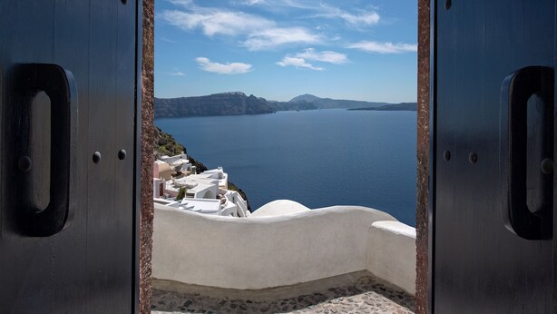 Vista a través de una puerta metálica, con un edificio blanco y una masa de agua al fondo.