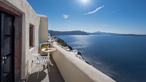 Un balcón con una mesa y sillas que da a un mar azul y montañas lejanas.