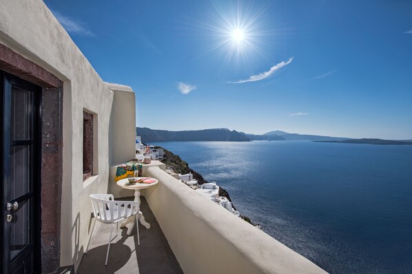 A balcony with a table and chairs overlooking a clear blue sea and distant mountains.
