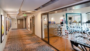 Passadís d'hotel amb un mosaic estampat, separadors de vidre i equipament esportiu.