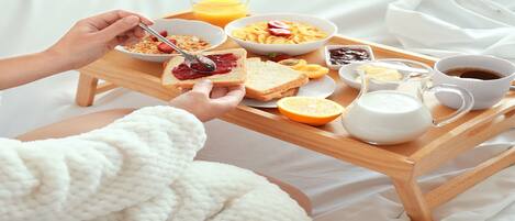 A breakfast tray with cereal, toast, fruit, and beverages on a bed.