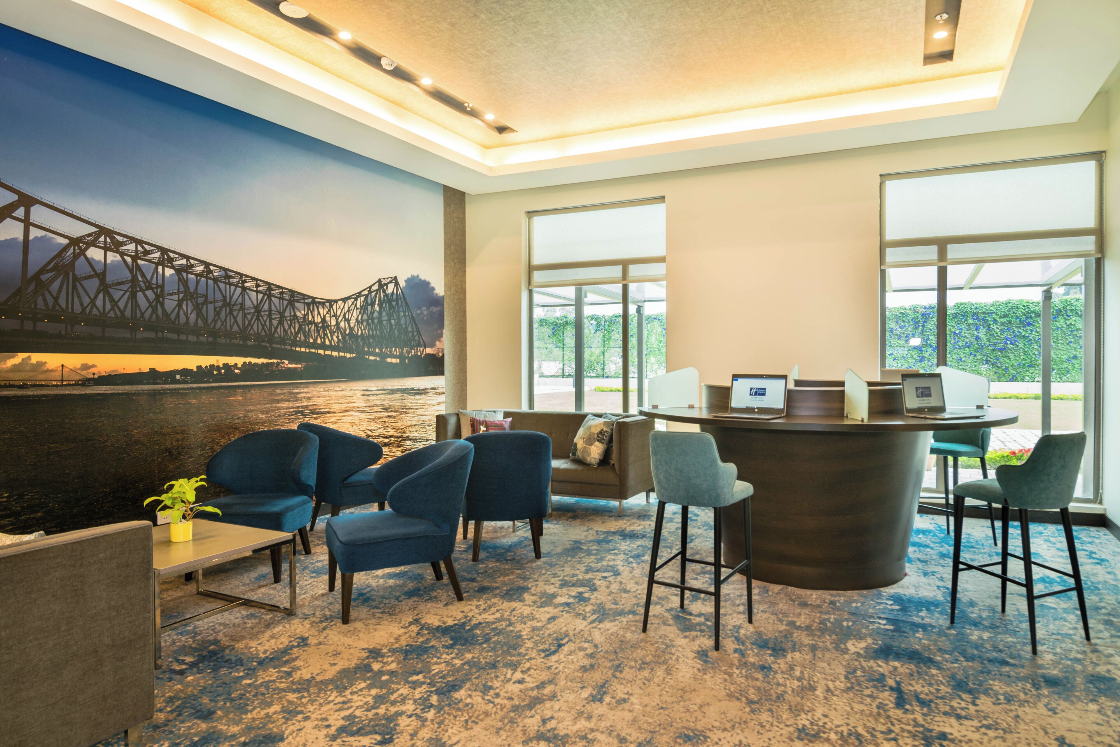 A modern hotel lobby with a large mural of a bridge, comfortable seating, and a reception desk with two laptops.