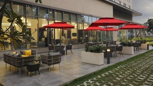 Zona exterior amb mobiliari de vimet i ombrelles vermelles, davant d'un edifici modern amb grans finestres.