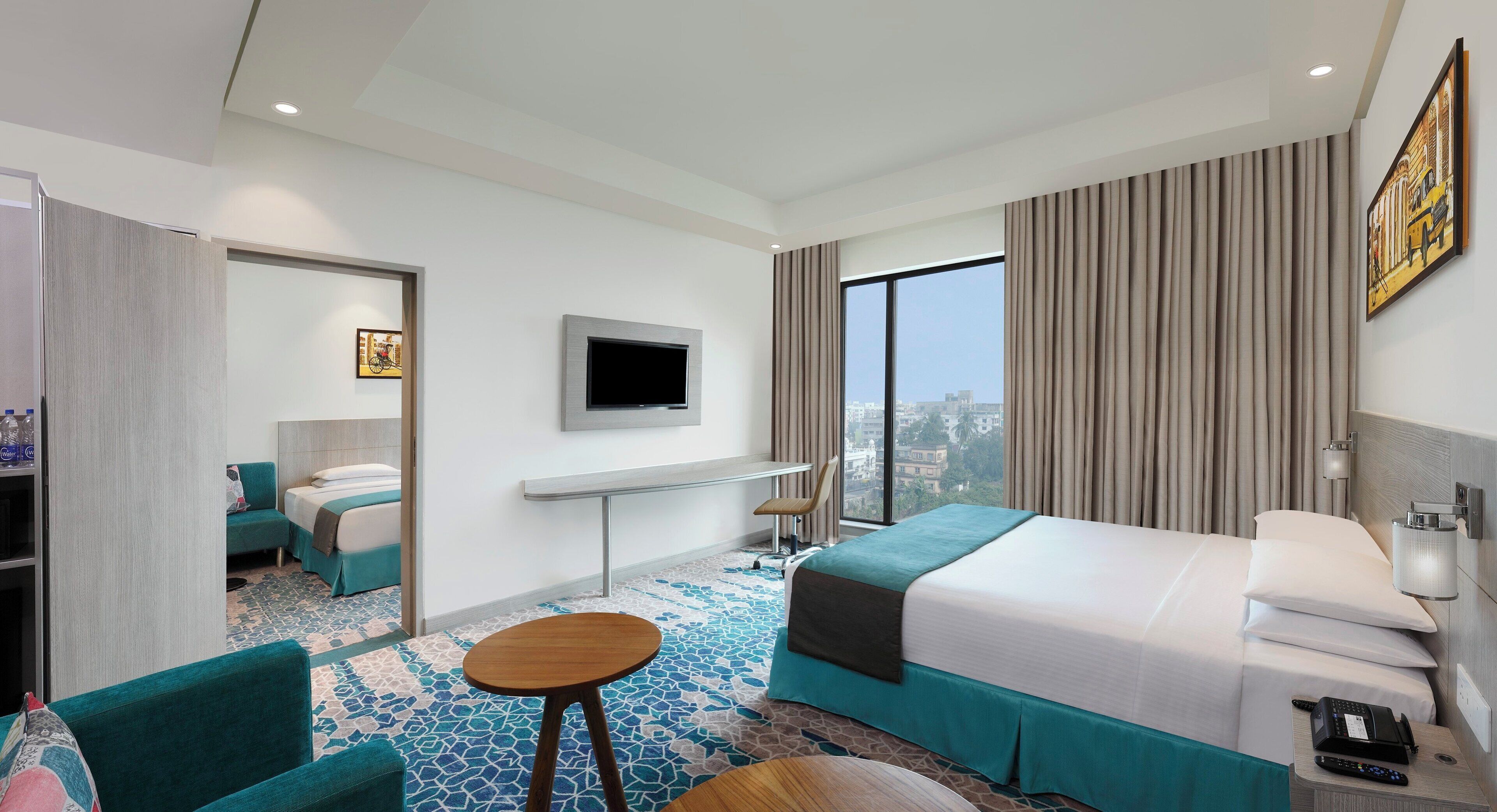 Une chambre d’hôtel avec un lit, un téléviseur fixé au mur, un bureau avec une chaise, une fenêtre avec des rideaux et une vue sur le paysage urbain.