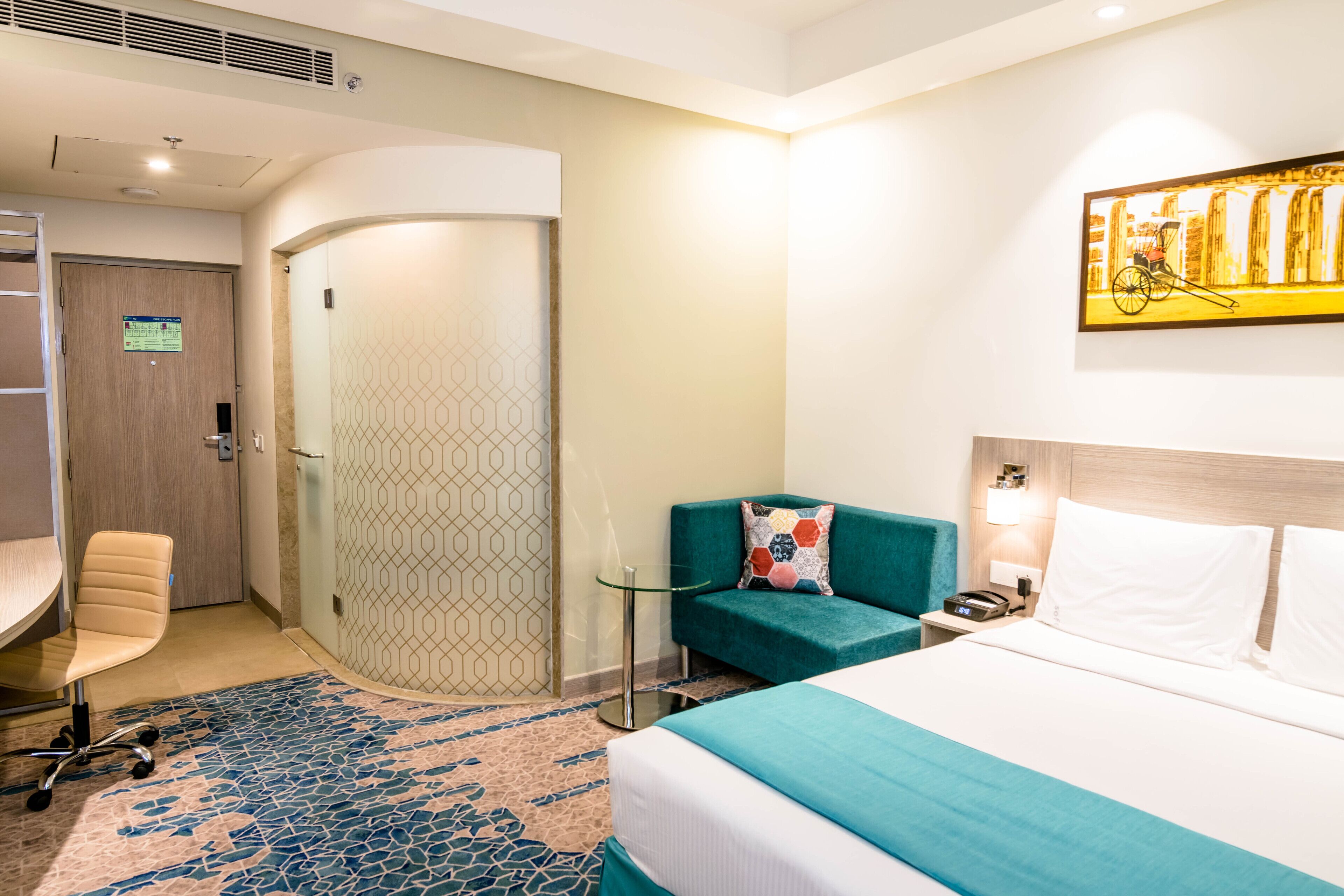 Een hotelkamer met een bed, een bureau, een stoel, een klein tafeltje en een aan de muur hangend kunstwerk.