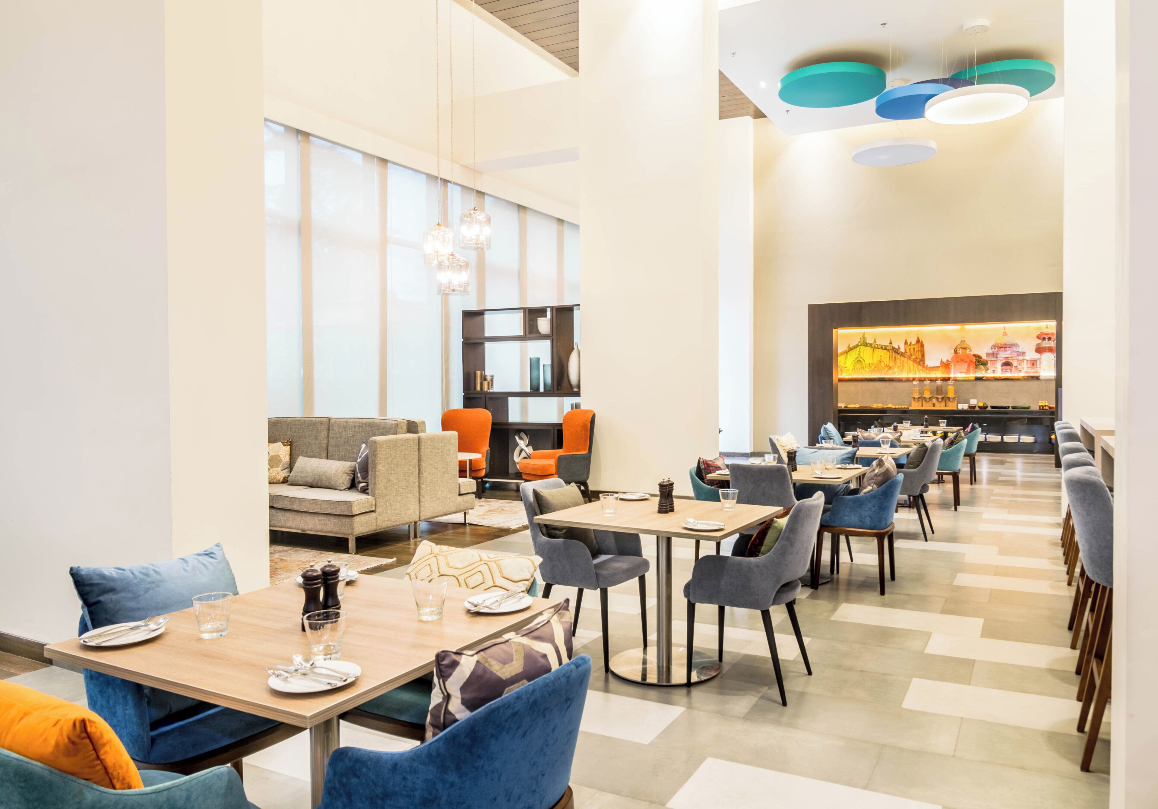 A modern dining area with multiple tables and chairs, a sofa, and a television screen displaying a cityscape.