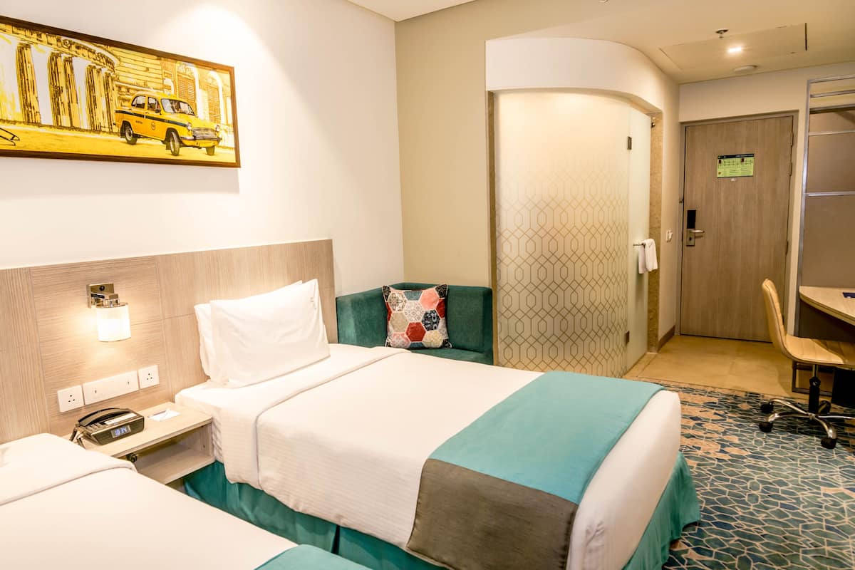Hotelkamer met twee bedden, een bureau, een stoel, een schilderij aan de muur en een deur met een bordje.