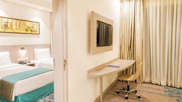 A hotel room with a bed, desk, chair, TV, and curtains.