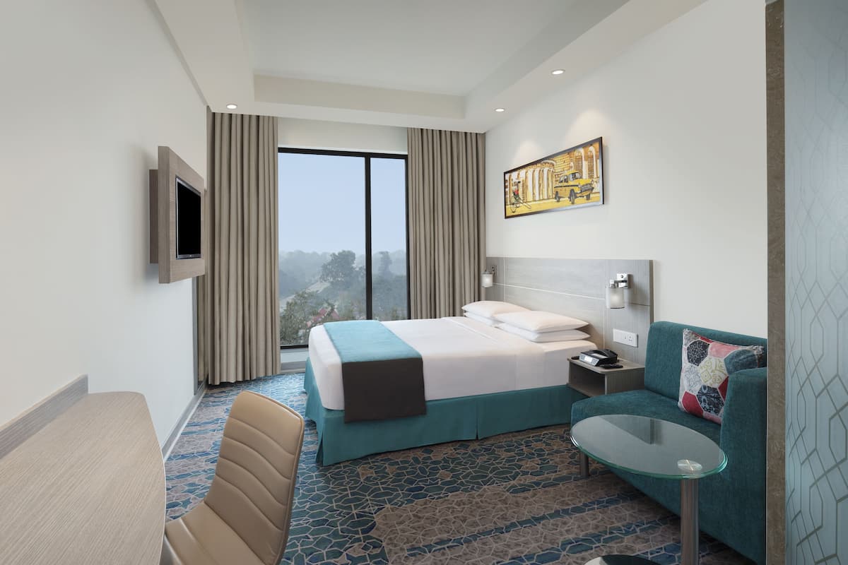 Een moderne hotelkamer met een groot bed, een glazen tafel, een bank en een tv die aan de muur is bevestigd.