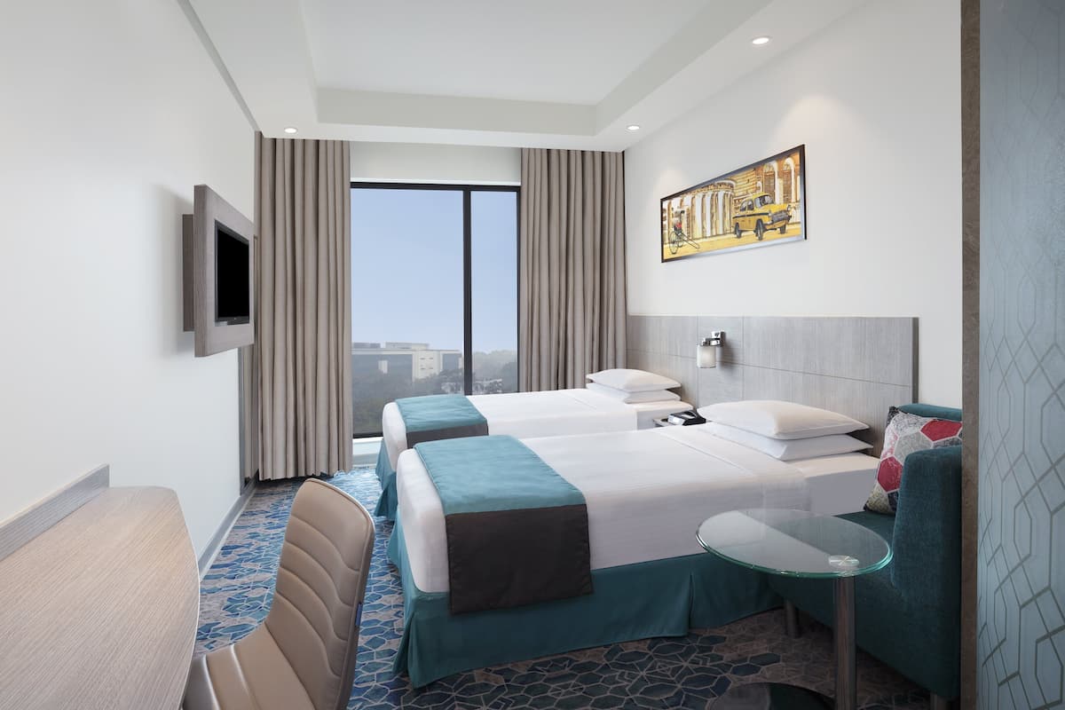 Een hotelkamer met twee bedden, een televisie, een tafeltje en uitzicht op de stad.