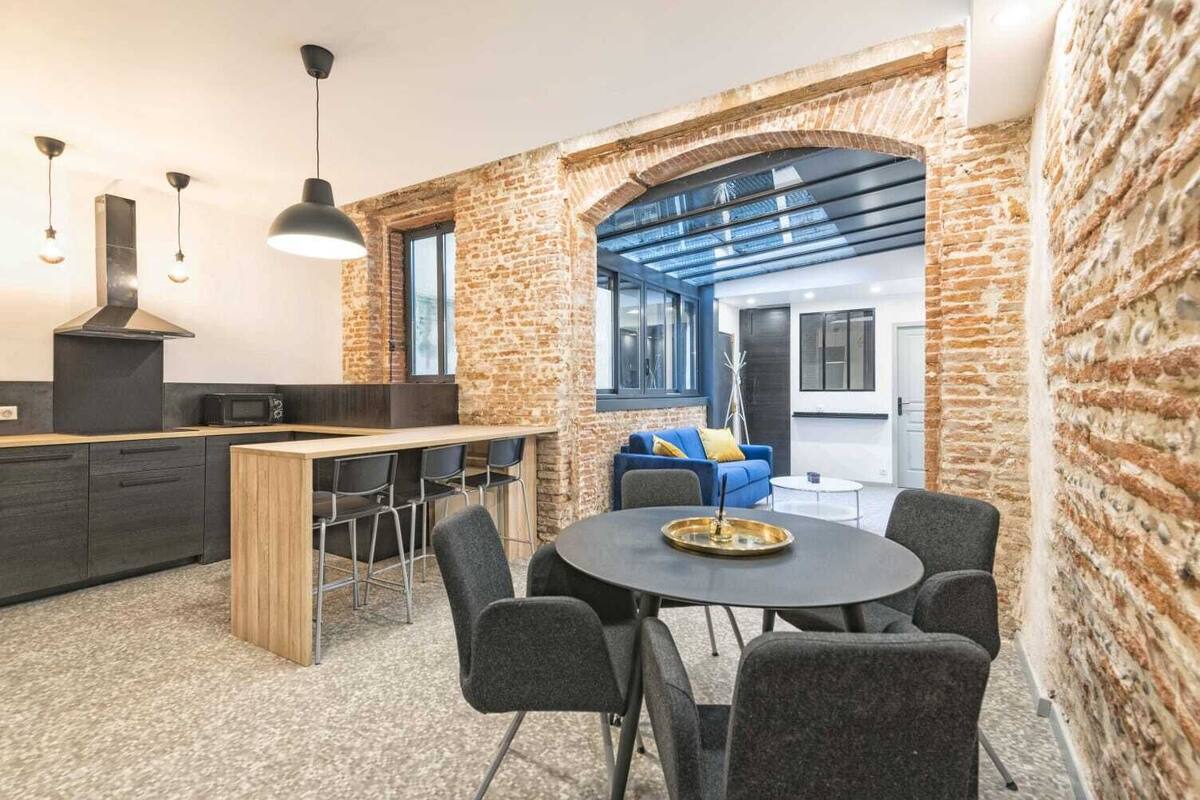 Eine moderne Küche mit Backsteinwand, einem Essbereich mit rundem Tisch und einem blauen Sofa.