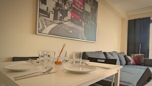 A dining area with a white table set for two, a framed black and white photo above, and a grey sofa in the background. - Harley Serviced Apartments - West Point (Sheffield)