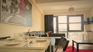 A dining area with a table set for two, a sofa, and a large window with curtains. - Harley Serviced Apartments - West Point (Sheffield)