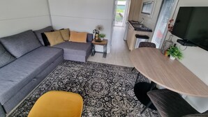 A compact living space with a grey sofa, a small dining table, and a TV mounted on the wall. - Houseboat Havana (Amsterdam)