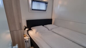 A single bed with a black headboard, a bedside table with a lamp, and a window with blinds. - Houseboat Havana (Amsterdam)