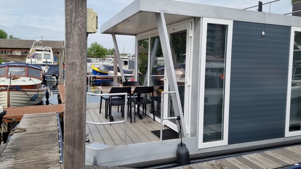 A modern outdoor deck with a table and chairs, overlooking a marina with boats. - Houseboat Havana (Amsterdam)