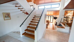 A modern interior with a wooden staircase, white walls, and a ceiling with wooden beams.