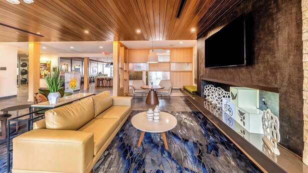 Un vestíbulo de hotel moderno con techo de madera, un televisor grande, un sofá, una mesa de centro y un piso con diseño.