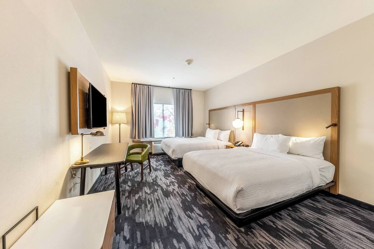 Una habitación de hotel con dos camas, un escritorio, una silla, un televisor y una ventana con cortinas.