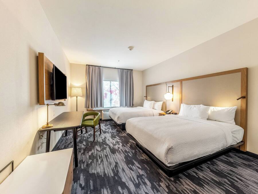 A hotel room with two beds, a desk, a chair, a TV, and a window with curtains.