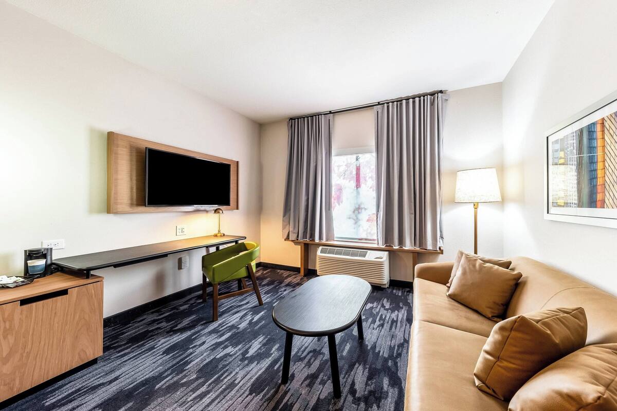 Habitación de hotel con televisión de pantalla plana, escritorio con lámpara, sofá y una silla.