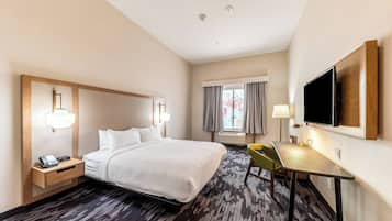 Een hotelkamer met een groot bed, een nachtkastje met telefoon, een bureau met stoel, een flatscreen televisie aan de muur en een raam met gordijnen.
