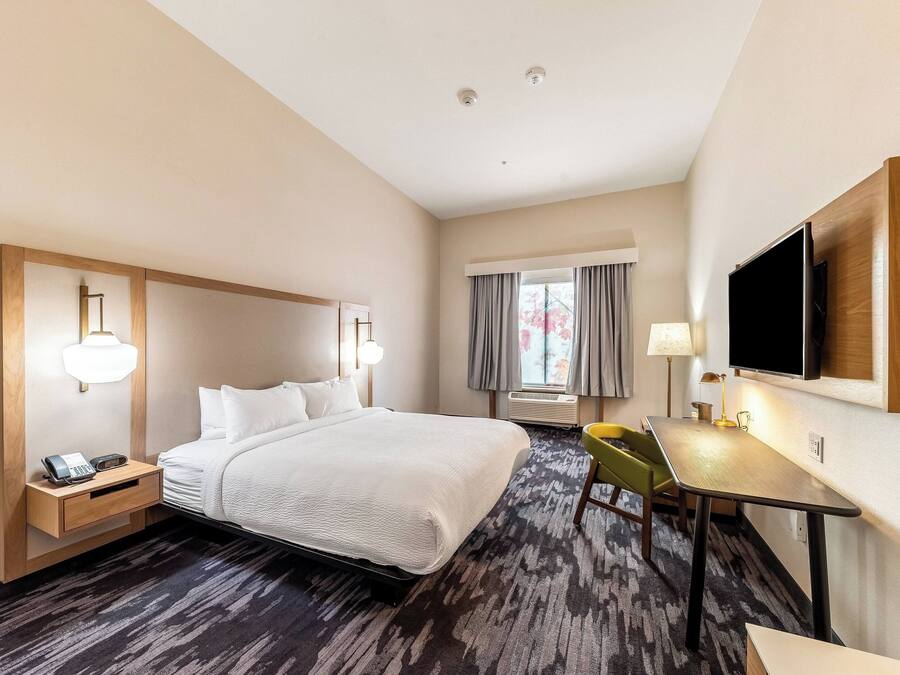 Een hotelkamer met een groot bed, een nachtkastje met telefoon, een bureau met stoel, een flatscreen televisie aan de muur en een raam met gordijnen.