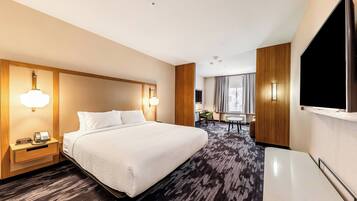A hotel room with a large bed, bedside tables with lamps, a flat-screen TV mounted on the wall, and a carpeted floor.