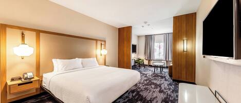 A hotel room with a large bed, bedside tables with lamps, a flat-screen TV mounted on the wall, and a carpeted floor.