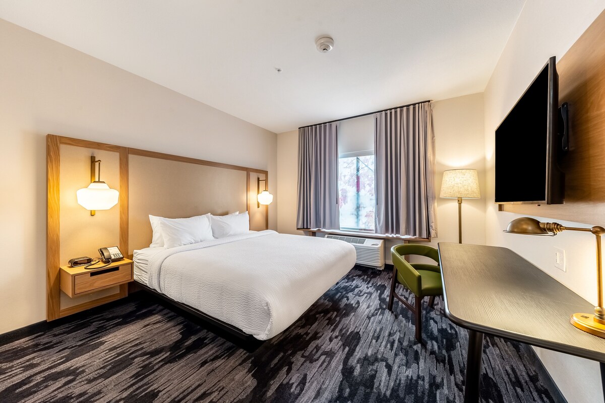 Een hotelkamer met een groot bed, nachtkastjes met lampen, een bureau, een stoel en een aan de muur bevestigde televisie.