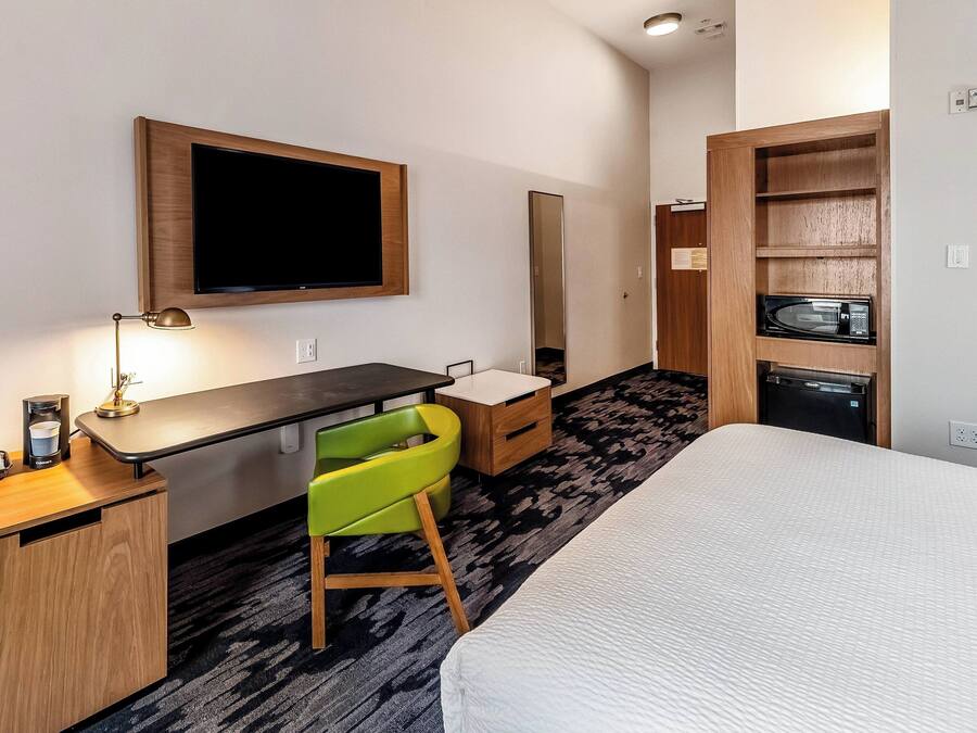 A hotel room with a bed, a desk, a chair, a TV, a mirror, and a microwave.