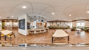 Un espacio interior amplio con techo curvo, una zona de bar central, múltiples disposiciones de asientos y una mesa grande en primer plano.
