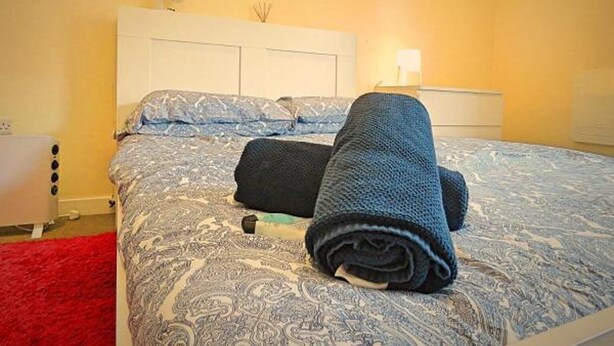 A neatly made bed with a patterned bedspread, a rolled-up blanket, and a bedside table with a lamp. - Fitzwilliam Street Rooms (Sheffield)