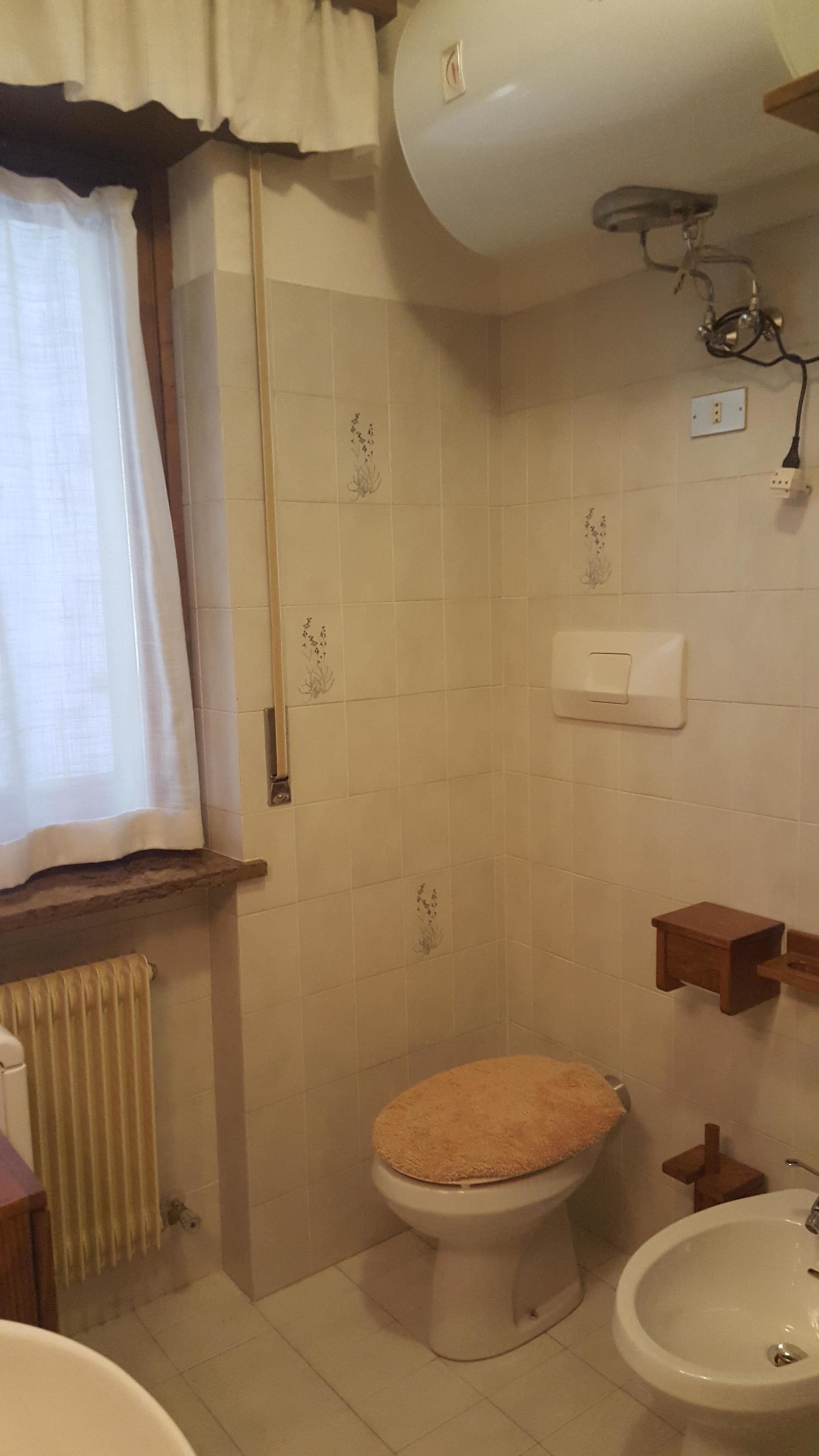 Un bagno con WC, bidet e una finestra con tende.